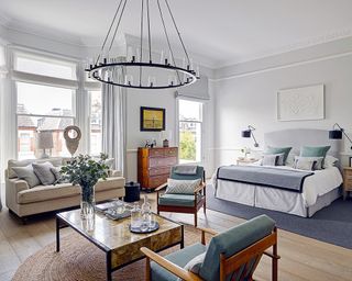 A white studio apartment with pale blue bed, sofa and armchairs around a walnut coffee table.