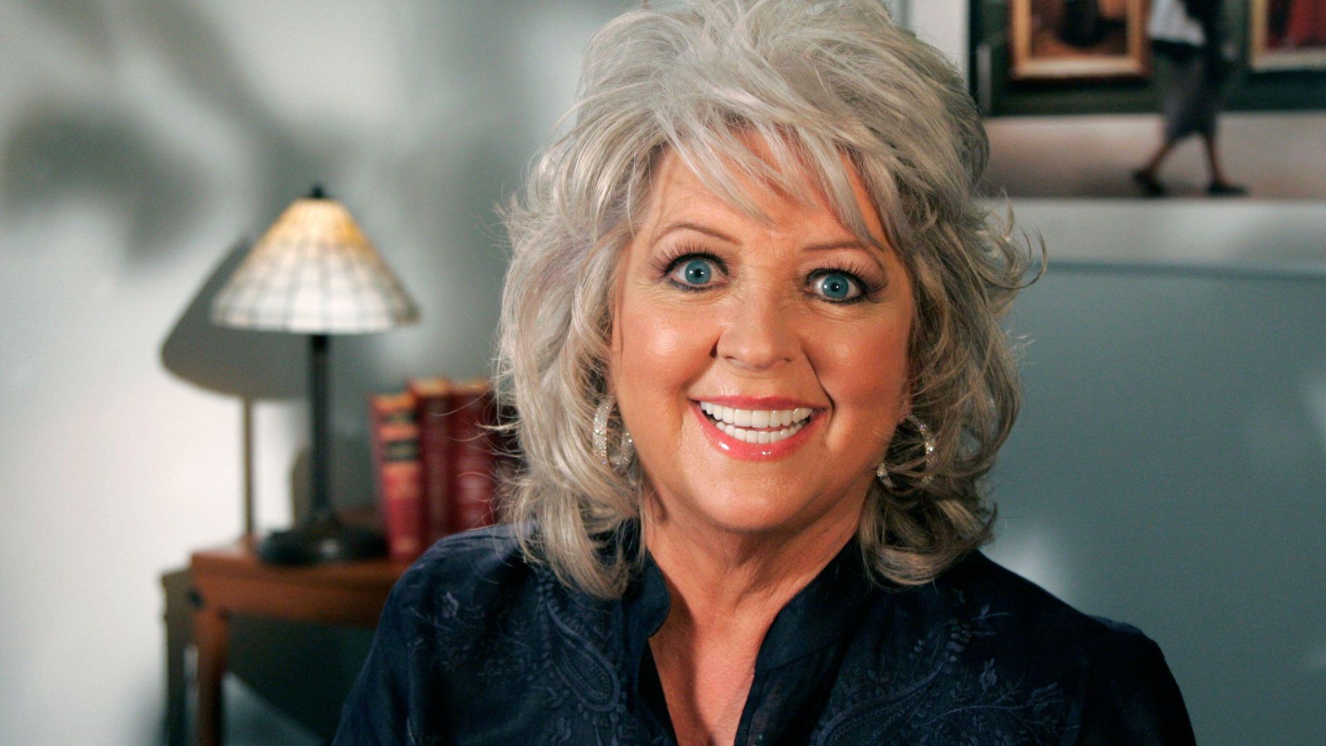 Paula Deen smiles in front of a lamp and some books