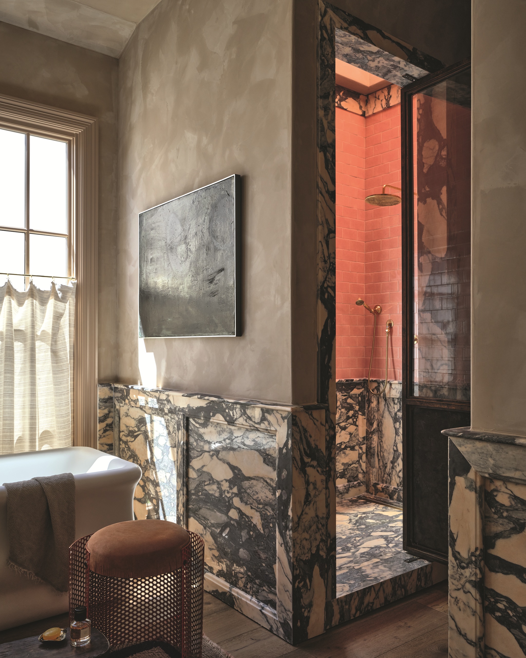modern bathroom with brown rendered walls, marble detailing, stool, freestanding bath, cafe curtains, and an enclosed shower with papaya-colored tiles
