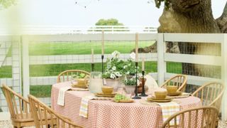 A table outside laid with a gingham tablecloth, tapers, yellow bowls, and napkins