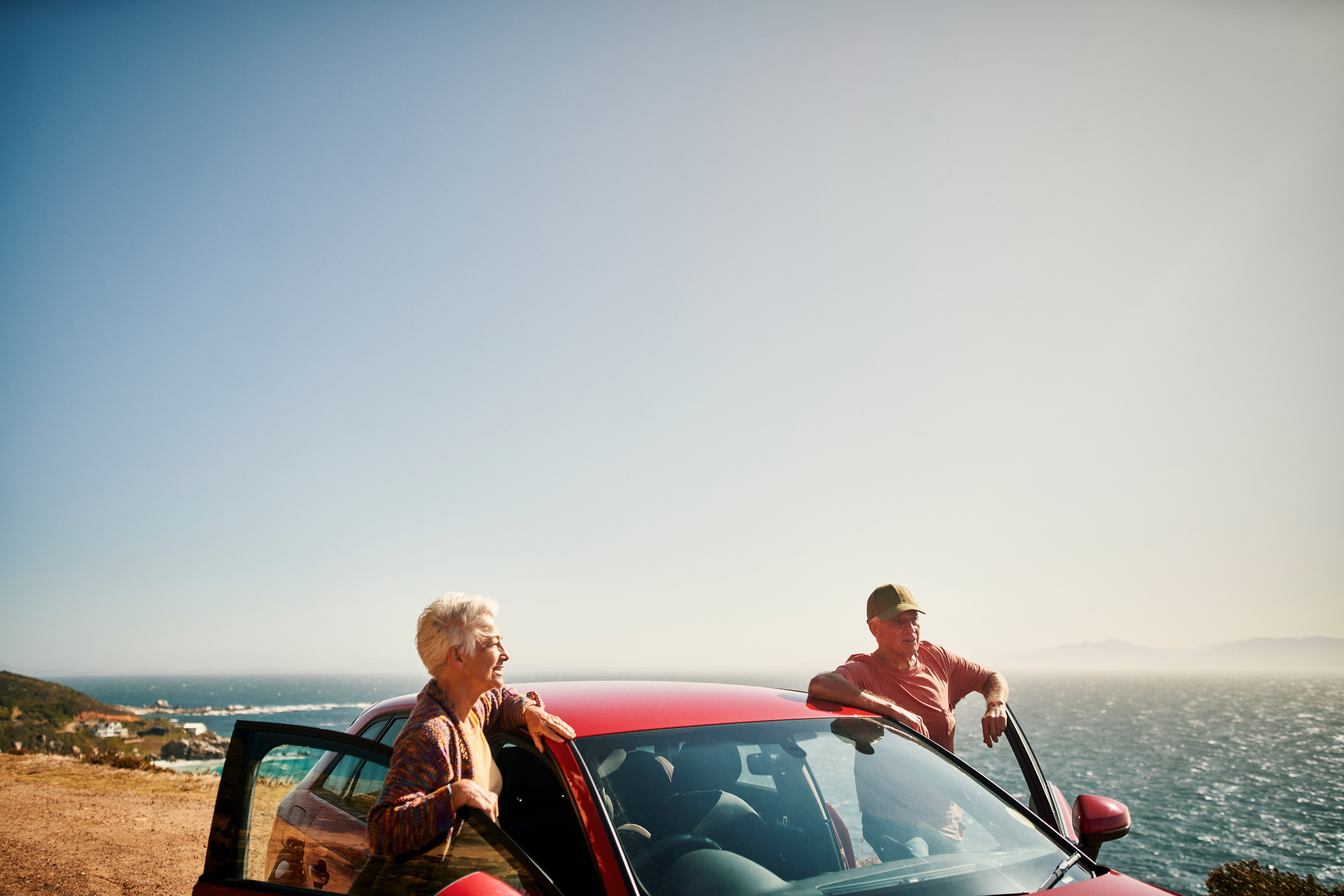 A senior couple standing beside car at a scenic outlook.
