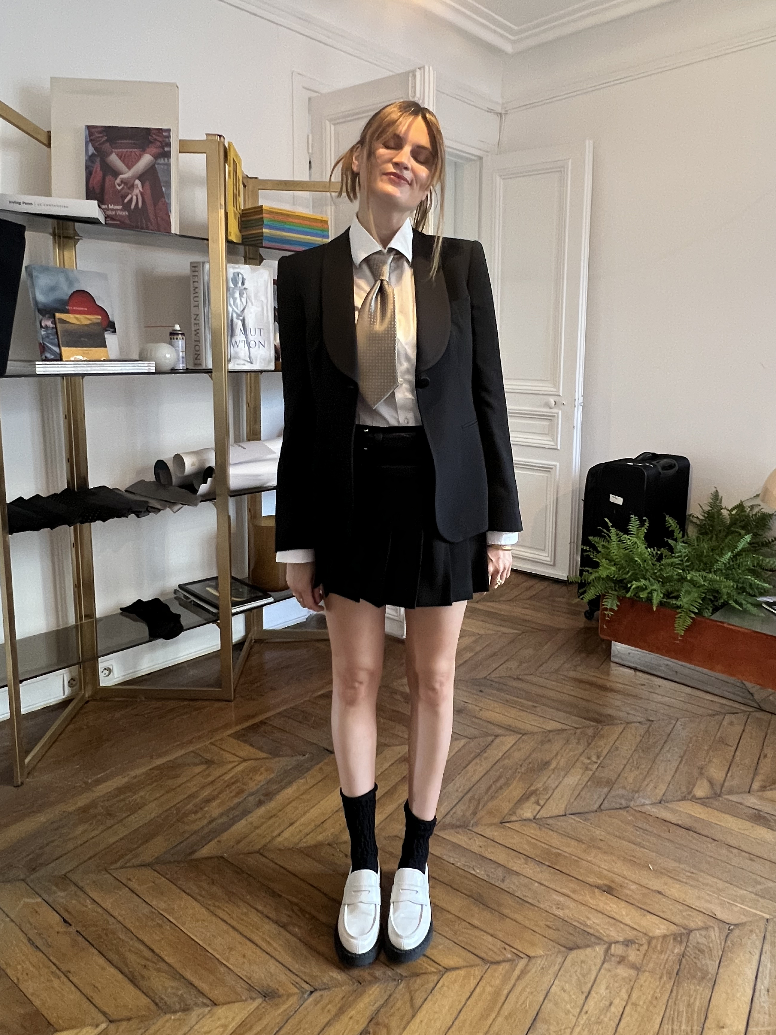 French editor Eugenie Trochu wearing a black blazer, with a button-down and tie, a black pleated mini skirt, black socks and platform white loafers