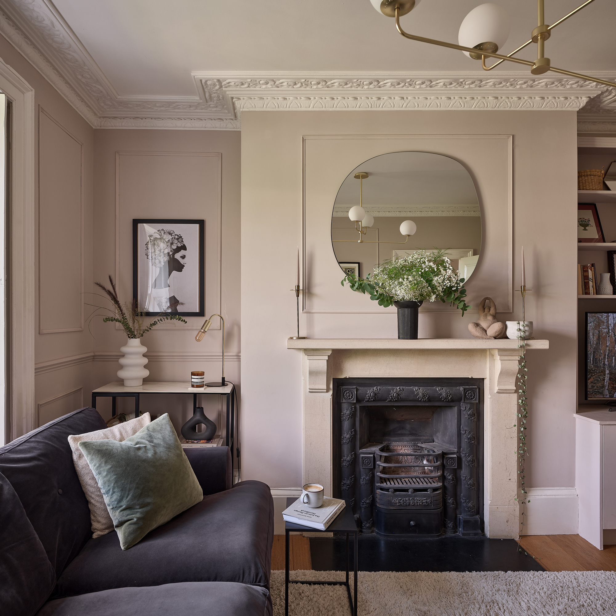 a pale pink living room with a dark purple velvet sofa fireplace and classic cornicing
