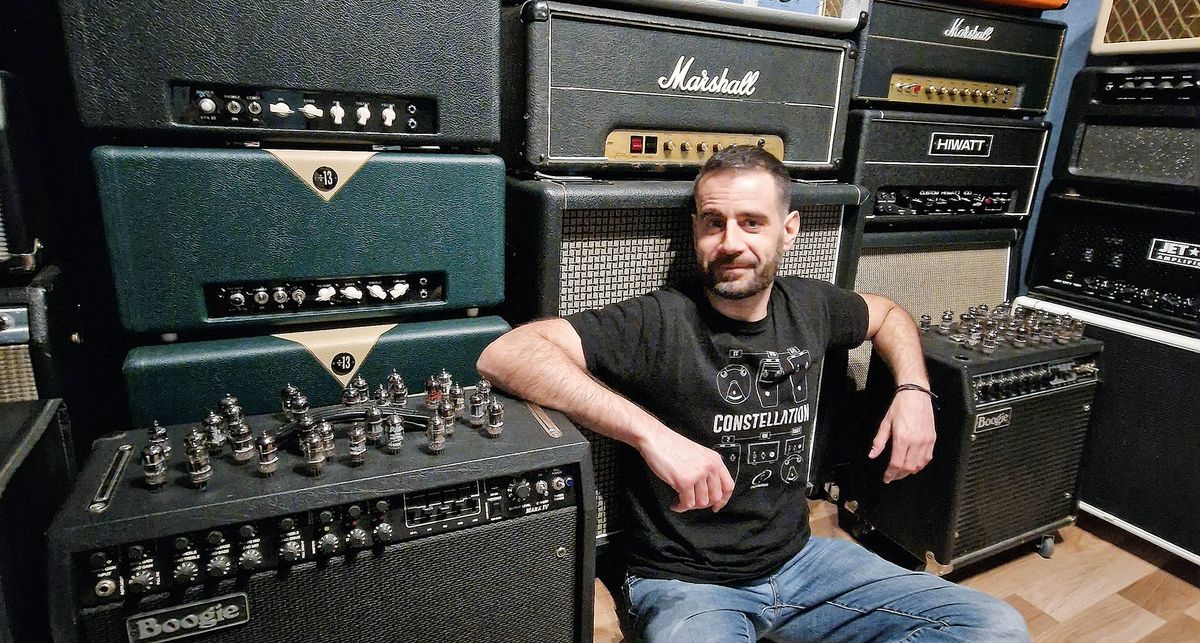 Crazy Tube Circuits&#039; Christos Ntaifotis sits in front of his amp collection, with Boogies to his left and right and Marshalls and HiWatts behind him