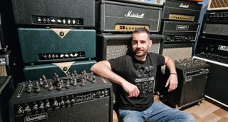 Crazy Tube Circuits' Christos Ntaifotis sits in front of his amp collection, with Boogies to his left and right and Marshalls and HiWatts behind him.