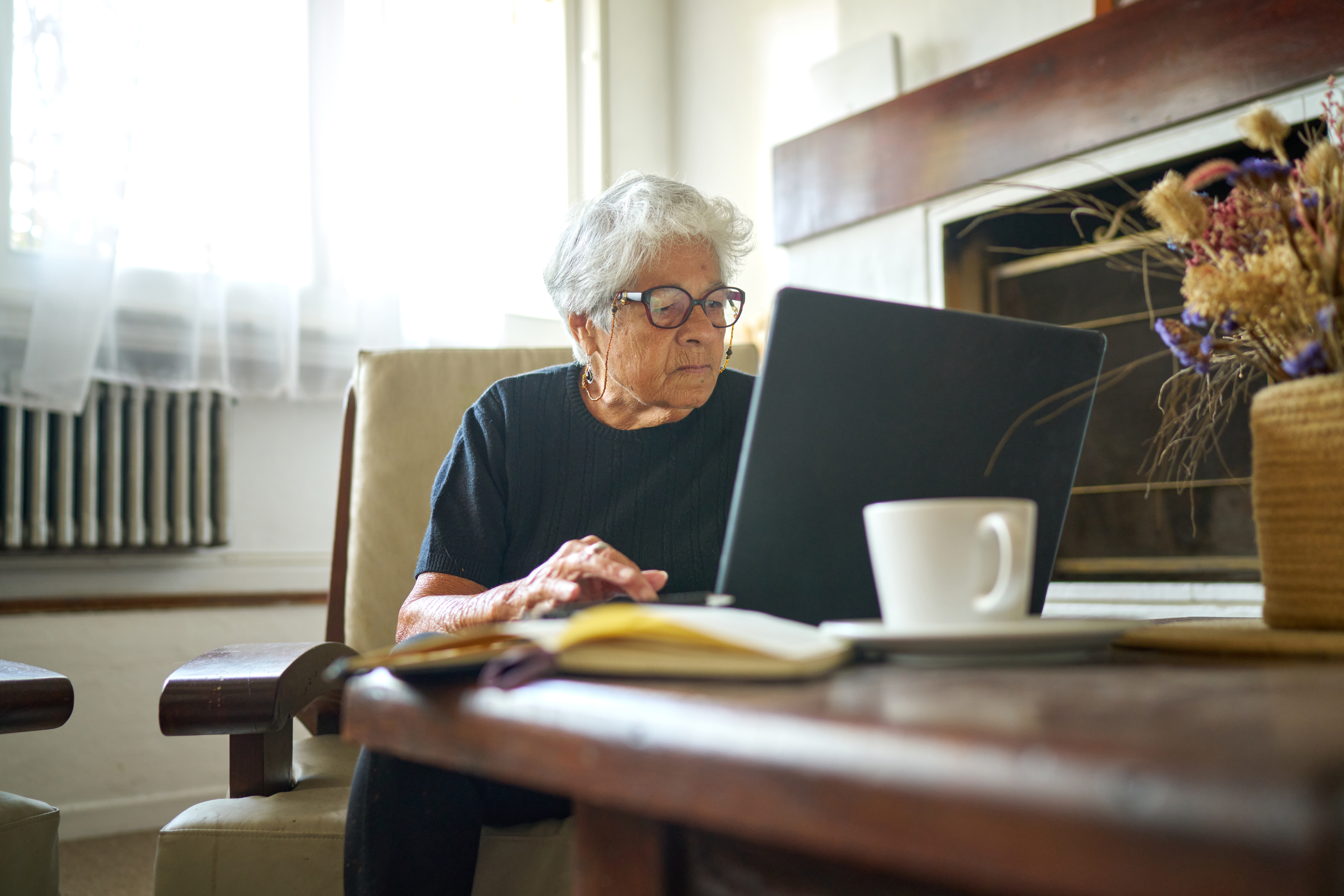 Older woman using laptop alongside open notebook