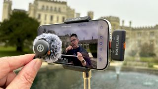 A hand holds the transmitter with a fluffy wind shield attached to the mic