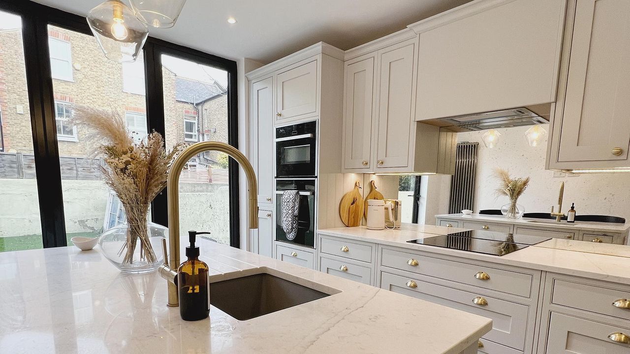 neutral kitchen with mirrored splashback and gold tap on a large island unit