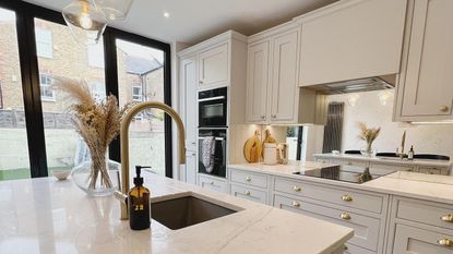 neutral kitchen with island unit and gold tap, plus mirrored splashback 