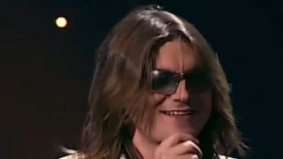 A close up of Mitch Hedberg smiling and telling a joke on stage