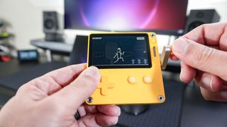 Playing a crank-based game on the Playdate handheld in front of a desk setup