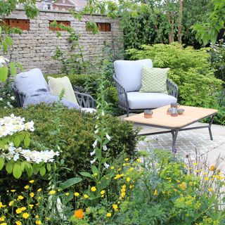 A pair of garden armchairs nestled amongst green borders in a garden
