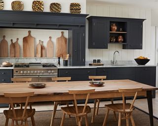 Dark kitchen cabinetry with a large wooden dining table and chairs and an assortment of coordinating wooden chopping boards on display.
