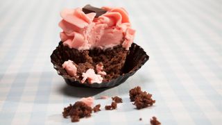a half eaten chocolate cupcake with pink frosting sitting on a table