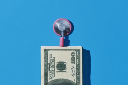 closeup of a pink stethoscope and a pile of fake US dollars, on a blue background