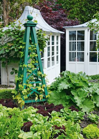 small garden ideas with a vegetable patch with green wooden obelisk, and white-painted sheds