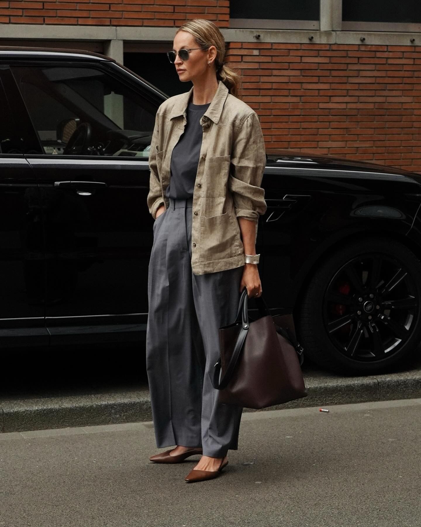Influencer @anoukyve wears brown heels with grey trousers and a khaki jacket.