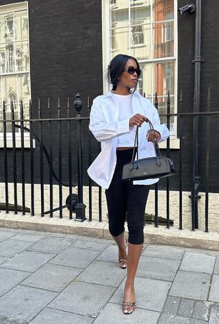 woman wearing capri pants with a white t-shirt, a white button-down shirt, black mules, and a black shoulder bag