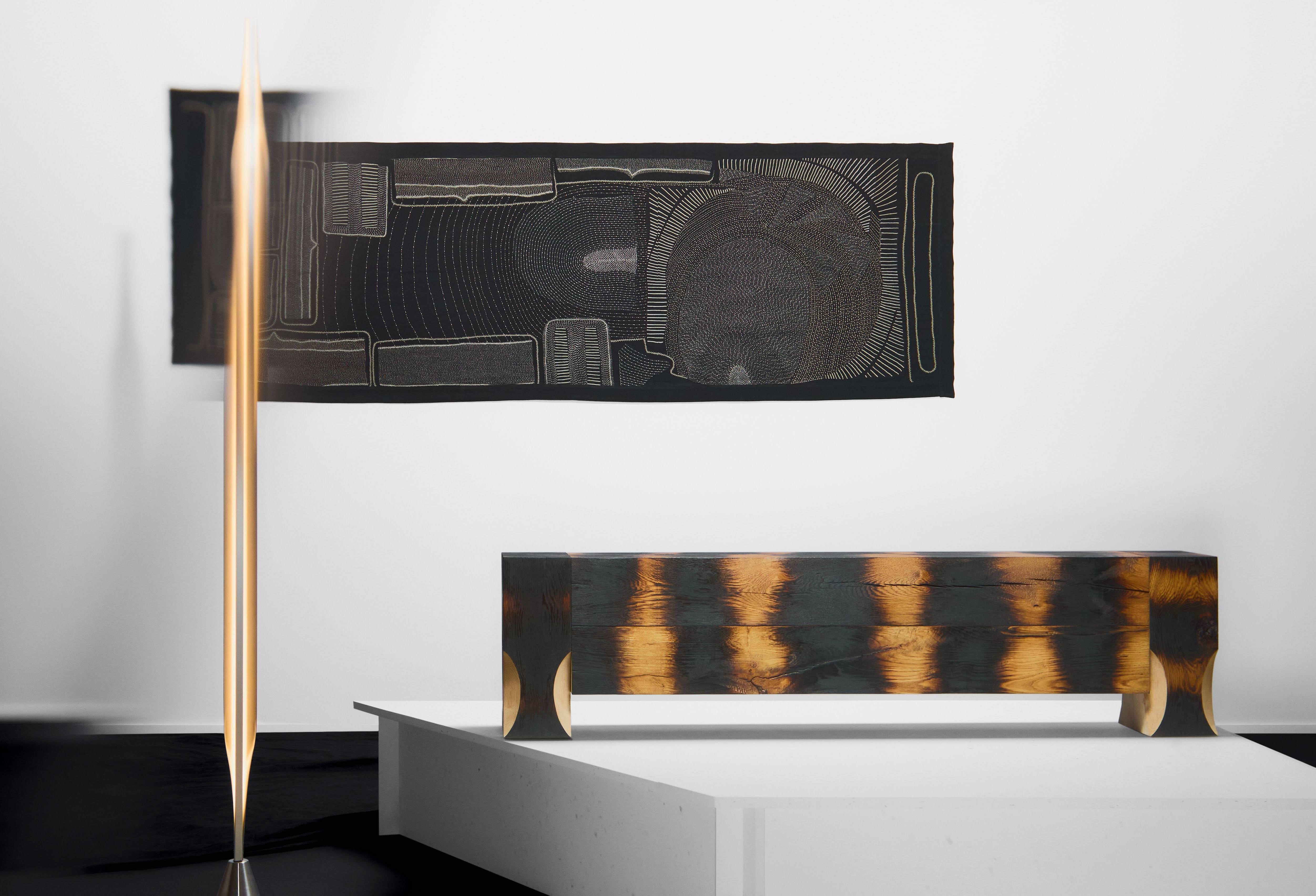 A minimalist lamp designed by Tokyo-based designer Kodai Iwamoto, showcasing the beauty of carved and hammered aluminum, positioned alongside a sculptural piece.