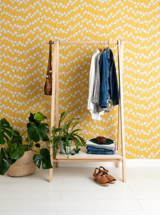 yellow wallpapered wall featuring retro print, and wooden hanging rail, and potted plants.
