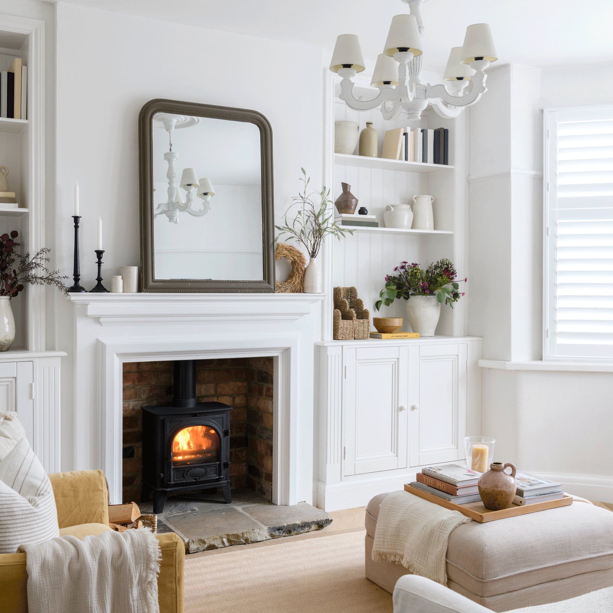 a neutral living room with a fireplace and woodburner, overmantel mirror and fitted alcove shelving