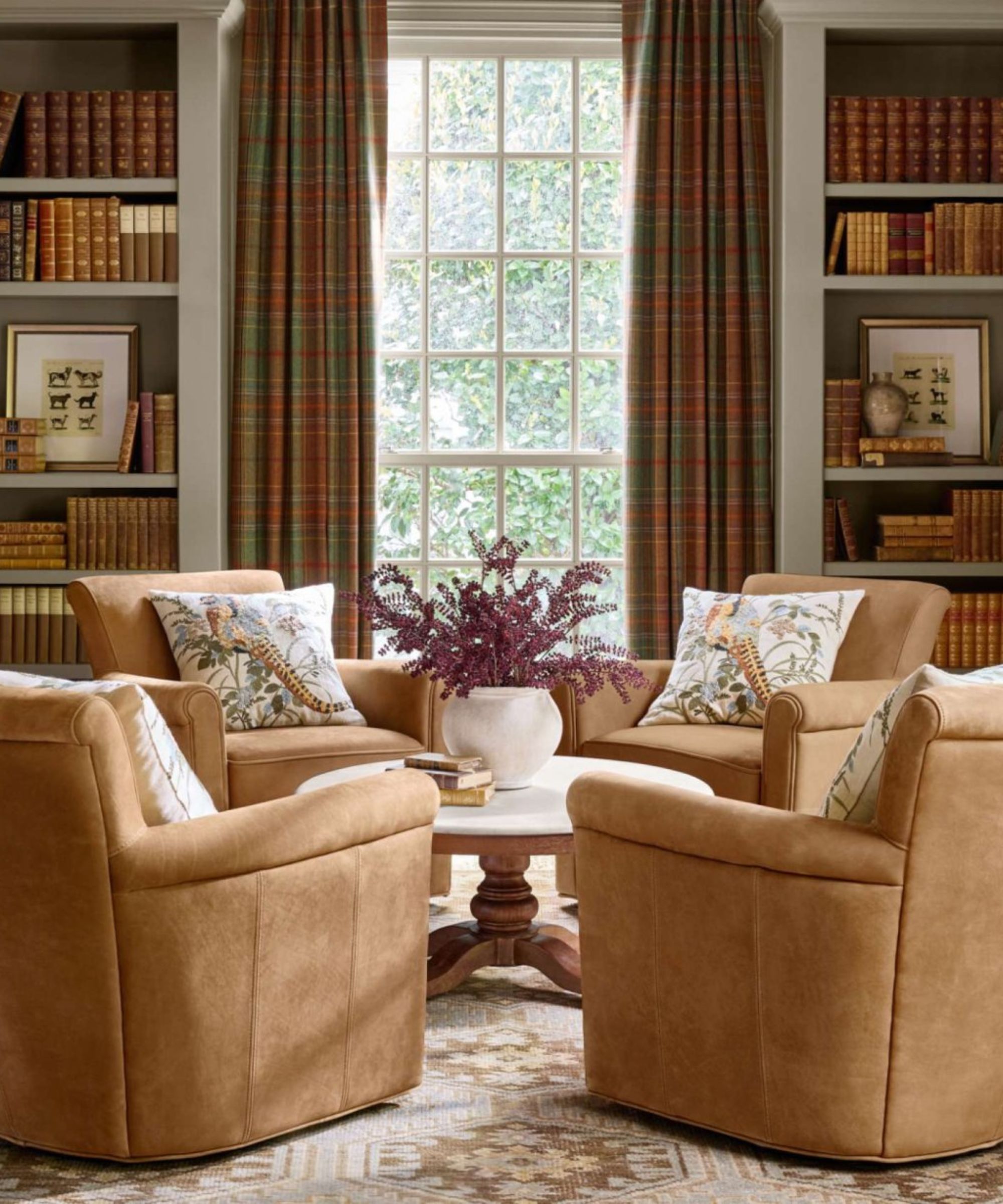 Living room with a fall feel. Four brown chair sit in the middle around a white and wood coffee table and the far wall has a large window and build in bookcases either side. The window is dress in plaid orange and green drapes