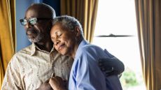 Senior married couple embracing in front of window at home
