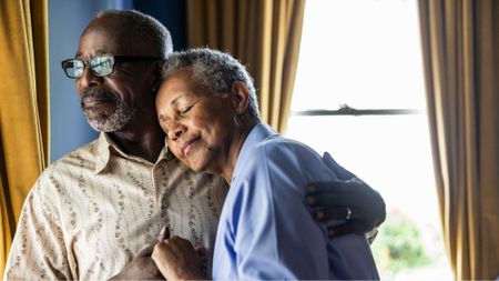 Senior married couple embracing in front of window at home