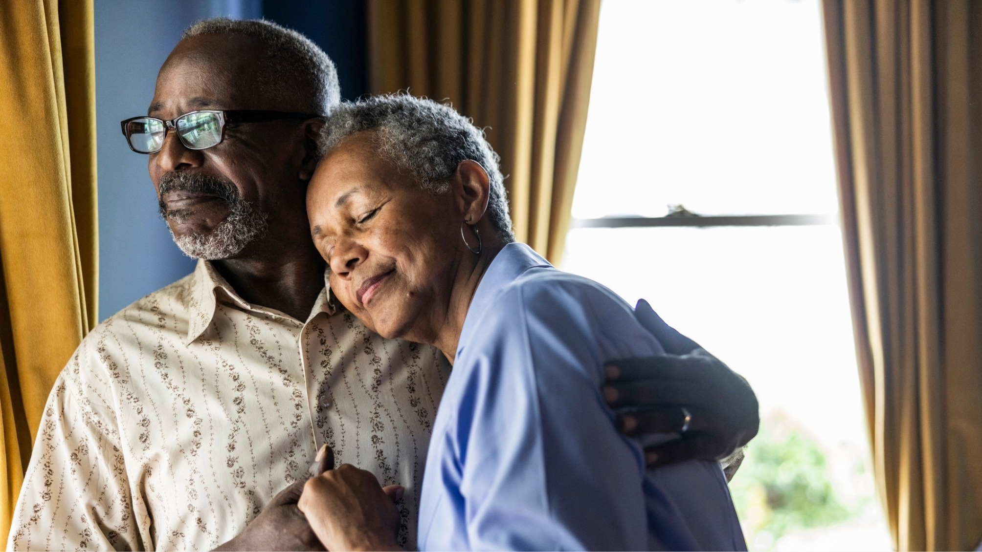 Senior married couple embracing in front of window at home