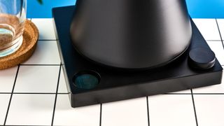 the fellow Corvo EKG kettle in matte black photographed against a blue background with a glass mug and black and white table