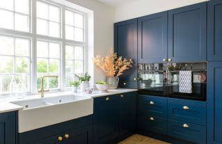 Dark blue kitchen with brass handles and a large butler's sink and large window