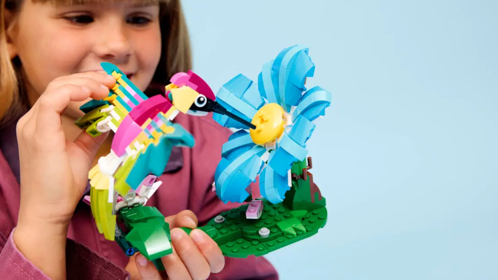 A child smiles while holding up a Lego hummingbird and flower