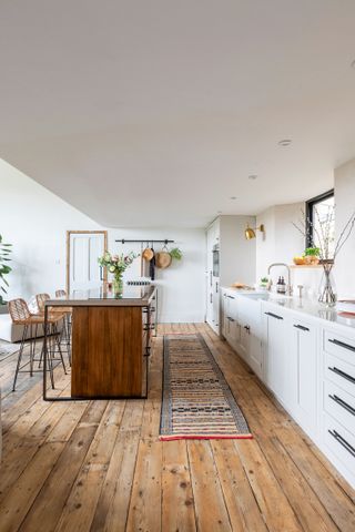 A white kitchen with runner rug, wooden island and wooden flooring