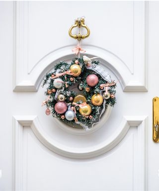 A Christmas crown hanging on a white front door with molding