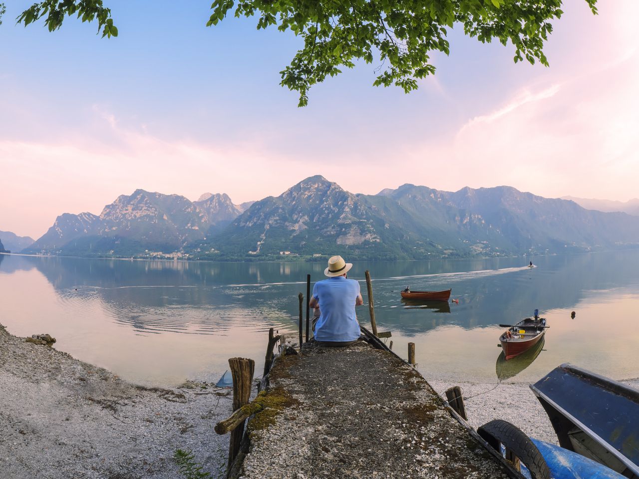 A person sitting alone on the edge of a pier looking at a beautiful mountain scene