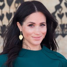 Meghan Markle looking at the camera in gold earrings and a teal dress