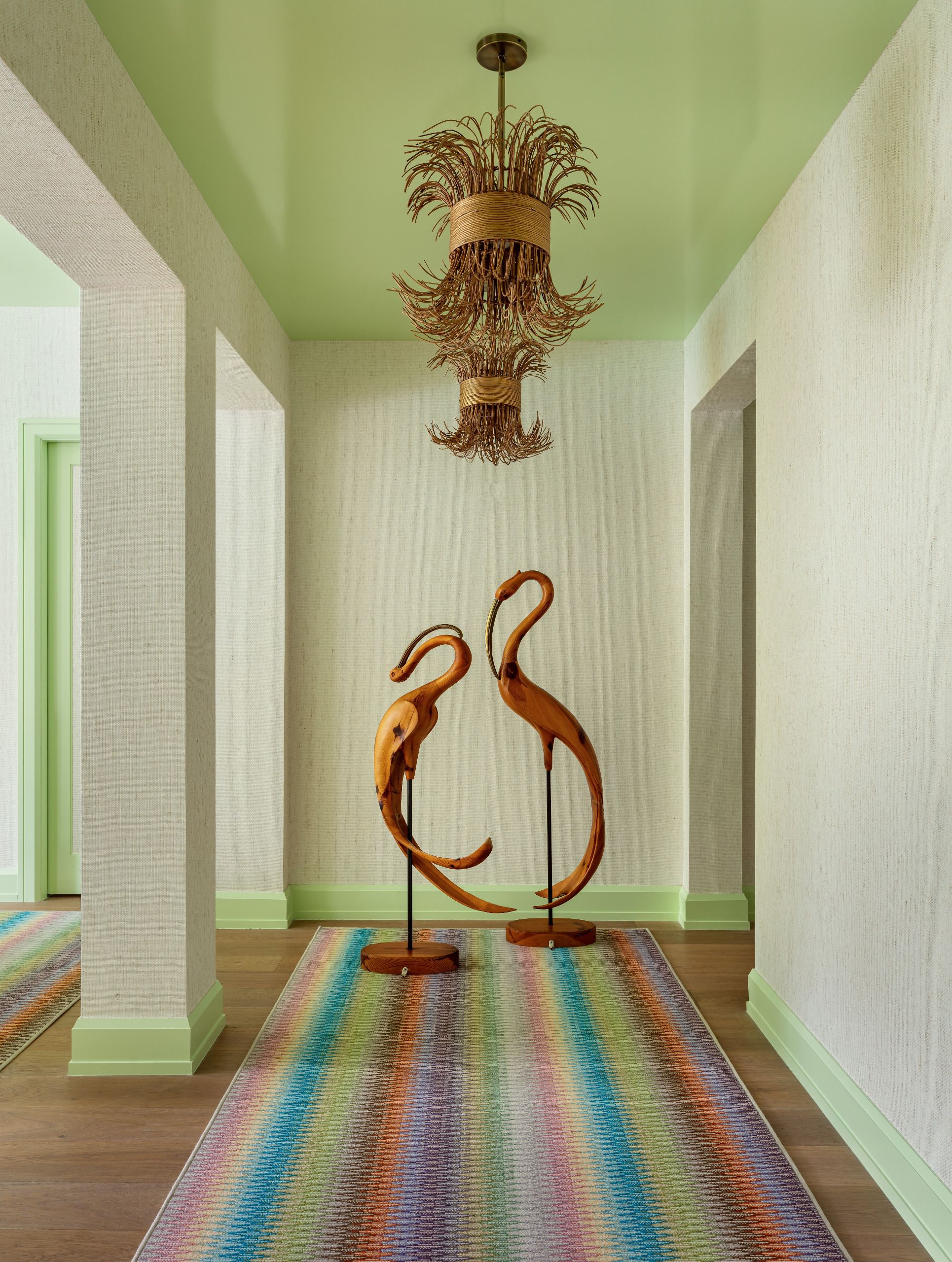 A hallway color-drenched in lime with gloss ceiling, contemporary light fitting and sculptural figures