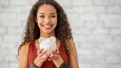 A teenage girl holds a piggy bank and smiles.