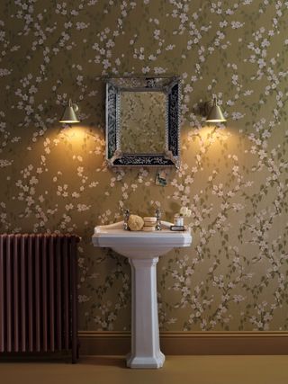 An example of traditional powder room ideas showing a dark mustard powder room with floral wallpaper and wall lighting