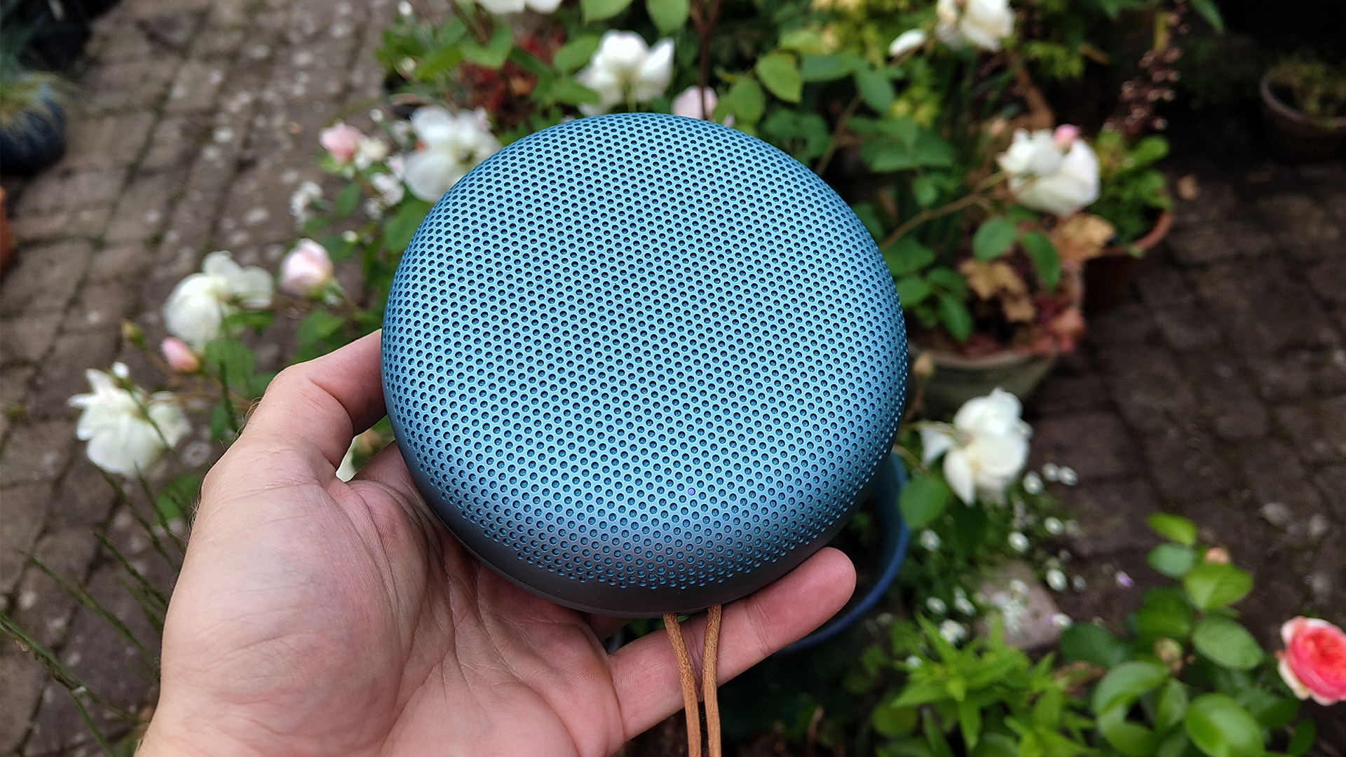 Bang & Olufsen Beosound A1 (3rd Generation) wireless speaker held in hand above white flowers