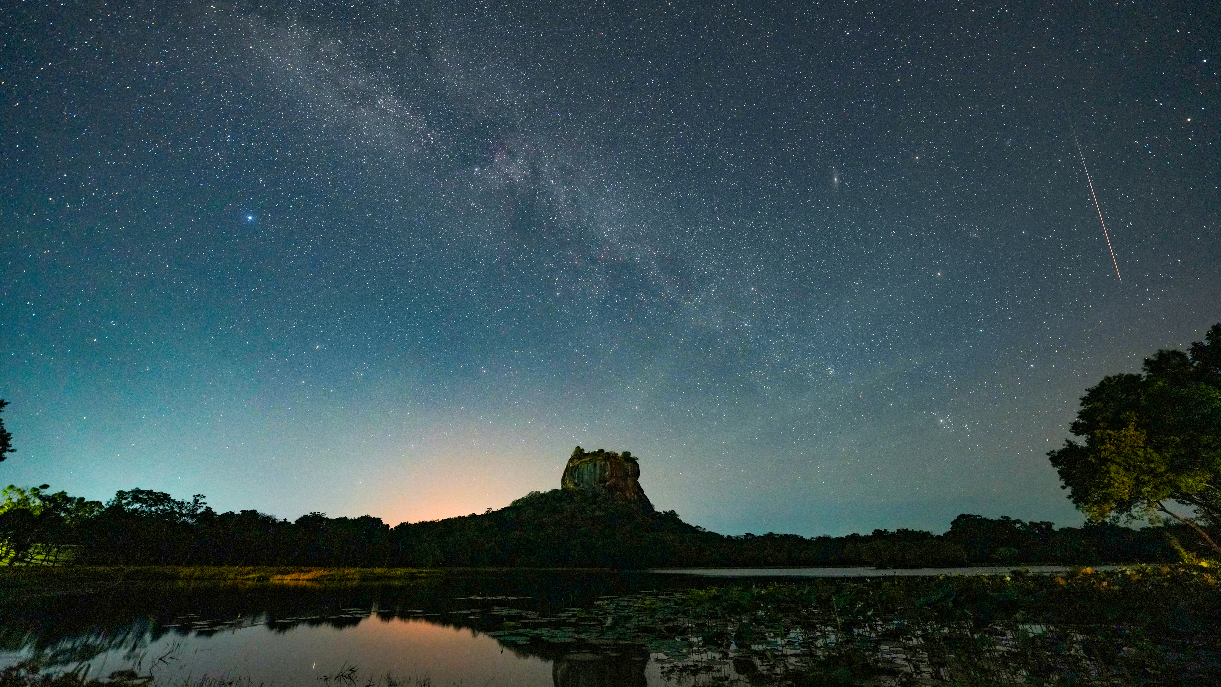 A Perseid meteor streaks across the Milky Way above the ancient Sigiriya Rock Fortress, a UNESCO World Heritage Site dating back to the 5th century, as its reflection is seen in still waters beneath a star filled sky in Dambulla, Sri Lanka, on July 23, 2026. The Perseid meteor shower occurs each year as Earth passes through debris left behind by Comet Swift Tuttle. (Photo by Thilina Kaluthotage/NurPhoto via Getty Images)