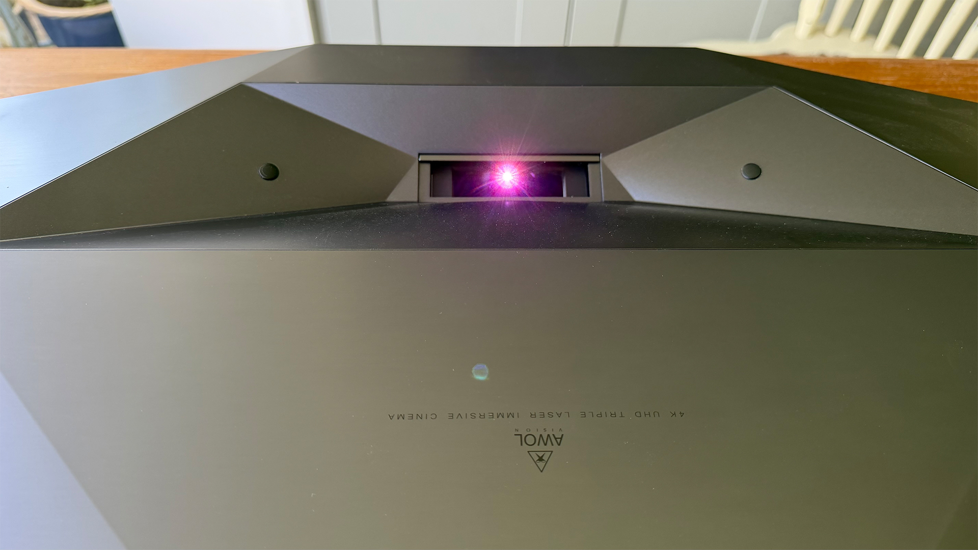 AWOL Vision Aetherion Max ultra short throw projector, close up on lens aperture with pink light shining from lens