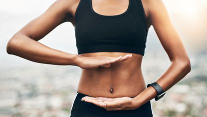 Woman in sportswear uses her hands to frames the section of her body where her gut lies