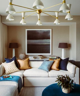 small living room with sectional and console table behind, large retro pendant, artwork, table lamps, round ottoman