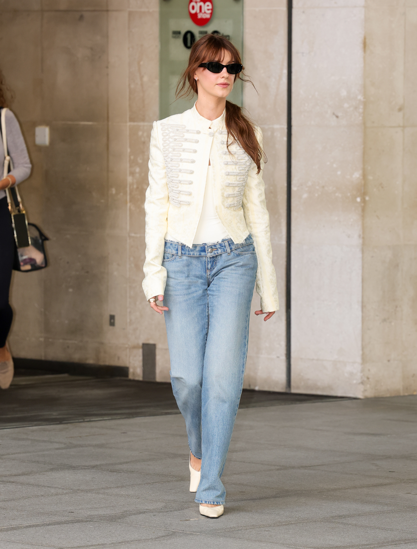 An image of Daisy Edgar-Jones wearing a Napoleon jacket with stovepipe jeans and white mules.