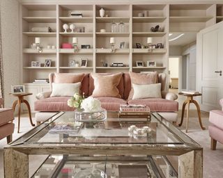 A pink sofa in front of white shelving and a glass coffee table