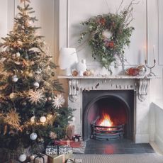 Living room with Christmas tree and wreath above log-burning fire.