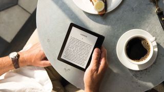 Jemand liest auf dem Kindle Oasis, während er an einem Tisch Kaffee trinkt