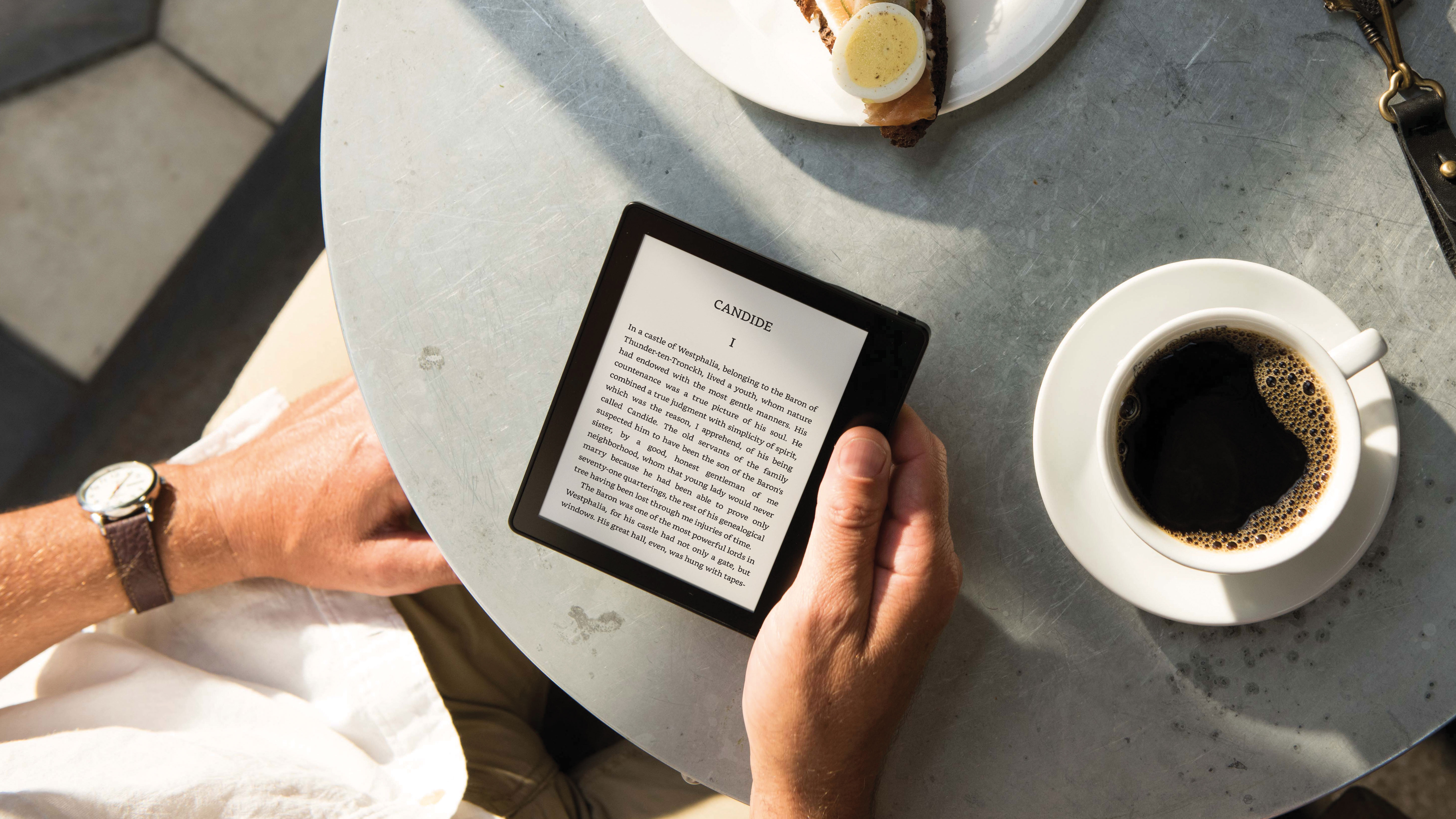 The Kindle Oasis being read as someone drinks coffee at a table