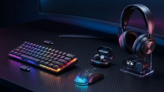 A sleek gaming setup with a colorful RGB keyboard, illuminated mouse, wireless earbuds, and headphones on a black surface, conveying a modern tech vibe.